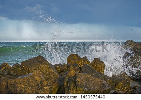 the storm begins at sea. the waves hit the rocks and the water is scattered. a sky covered with black clouds