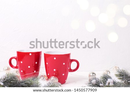 Fir tree spruces, red  dotted mugs or cups with hot  tea, coffee or cocoa and  silver garland  on white textured background.  Selective focus. Place for text.