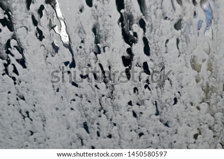 A car wash machine in action. White foam on the window of a car in a car wash.