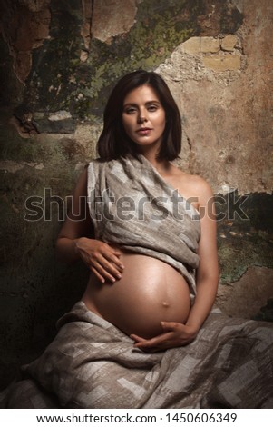 Art portrait of a beautiful pregnant woman. Old brick wall on the background. Linen fabric as clothing.