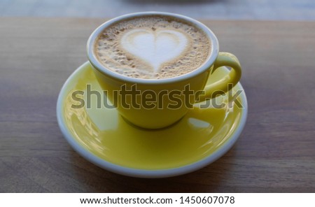 Macro photo cup of coffee cappuccino in yellow cup. Painted heart on skin coffee