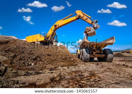 industrial excavator loading soil from sandpit into a dumper truck Royalty-Free Stock Photo #145061557