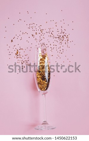 Star shaped golden confetti in a champagne glass on pink background. Festive party concept