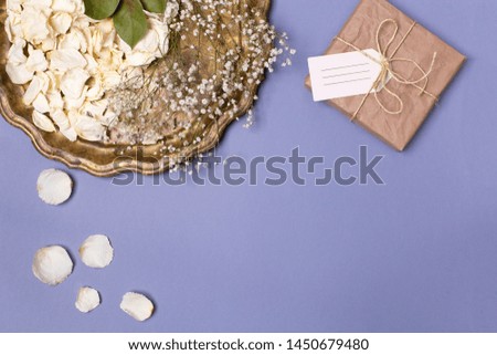 Autumn composition with dry petals of white roses and gypsophila on a beautiful vintage tray, a gift wrapped in craft paper on a blue background. Place for text.