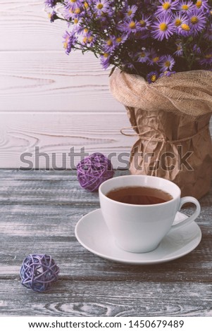 Romantic autumn composition with a cup of tea, lilac flowers in a vase on a gray wooden table. Autumnal concept.