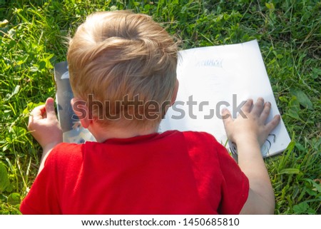 Boy reading a book. He lies on the grass on a Sunny day. Performs summer task for school.