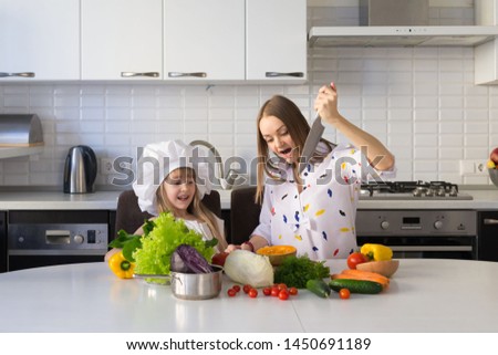 Beautiful mother and daughter, has happy fun smiling face, white chef hat. Cooks in kitchen appetizing tasty vegetables. Creative family concept. Cuisine food view. Woman portrait.