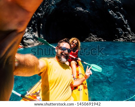 Happy cheerful people enjoying outdoor leisure activity in kayak on the coast ocean - selfie picture with nice couple - cave and ocean background and colors for vacation summer concept