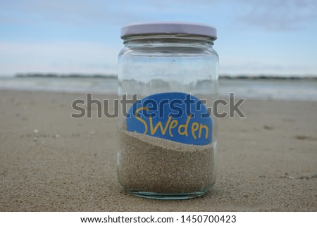 Souvenir of Sweden with a colored stone in a glass jar with sand on the beach