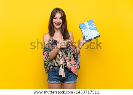 Caucasian girl in colorful dress over isolated yellow background holding gift box