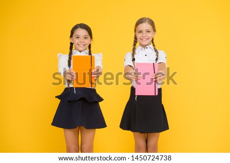 Sharing book love. Happy little girls holding books with colorful covers on yellow background. Cute small children smiling with encyclopedia or hand books. Educational books for pupils and students.