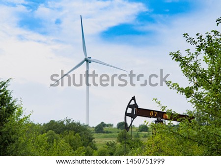 Operating oil and gas well, profiled on blue sky with clouds and wind turbine