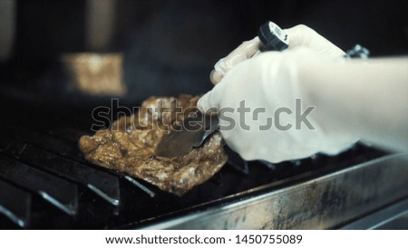 Close-up of chef's hands in white protective gloves grilling fresh, delicious steak on BBQ. Action. The concept of cooking in the restaurant.