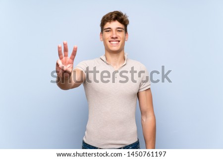 Handsome young man over isolated blue wall happy and counting three with fingers