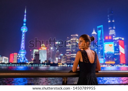Shanghai city night lights glowing in dark sky. Elegant lady by the Bund river in fancy lace dress evening gown. Asian model sightseeing.