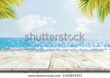 Top of wood table with seascape and palm leaves, blur bokeh light of calm sea and sky at tropical beach background. Empty ready for your product display montage.  summer vacation background concept.