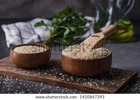 White sesame seeds in a wooden spoon on dark table, Sesame oil in jar and seeds concept, Sesame dark tone background. Royalty-Free Stock Photo #1450847393
