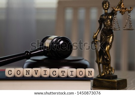 Word CONVICTION composed of wooden dices. Wooden gavel and statue of Themis in the background. Closeup Royalty-Free Stock Photo #1450873076