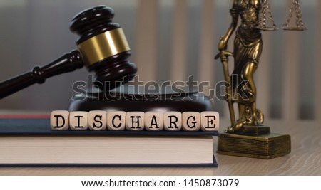 Word DISCHARGE composed of wooden dices. Wooden gavel and statue of Themis in the background. Closeup