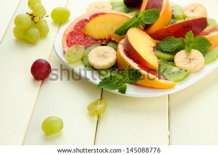 Assortment of sliced fruits on plate, on white wooden table