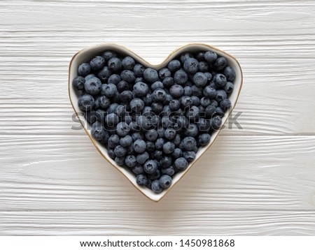 Blueberries in heart silhouette plate on wooden table. Top view. Food blogging concept. Horizontal photography.