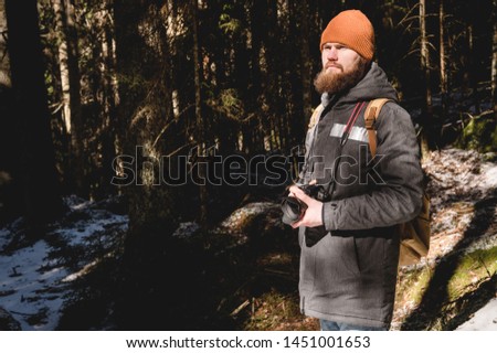 Portrait of a bearded photographer with a reflex camera in his hands in the winter coniferous forest. Photo travel concept