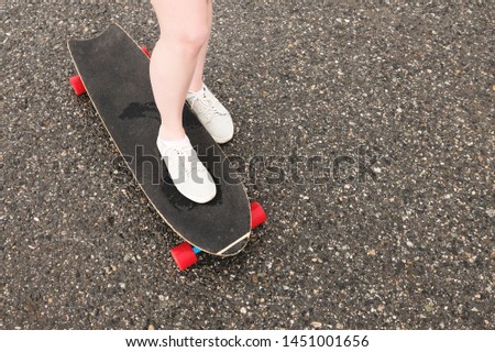Close-up of female legs in rag sneakers on a longboard on the background of asphalt at sunset. Big skateboard with girl legs. Youth leisure concept