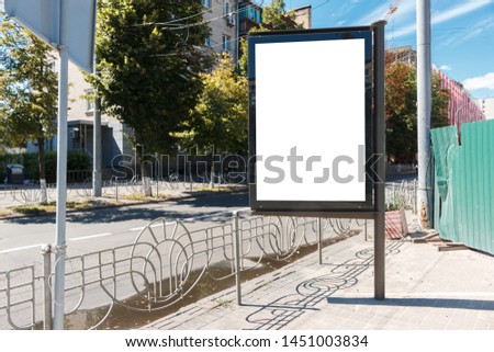 citylight with blank screen stands on the empty street near a construction site. empty white vertical billboard near the fence and pedestrian road. blank street poster or a lightbox with mock up space