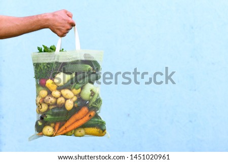 Eco friendly reusable shopping bag filled with fresh farm vegetables on a blue background. 