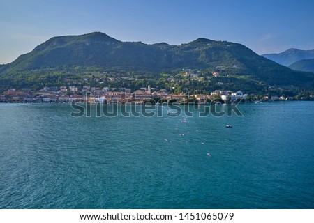 Swimmers swim in the open water against the background of the small town of Salo located on Lake Garda, Italy. Aerial photography with drone. 