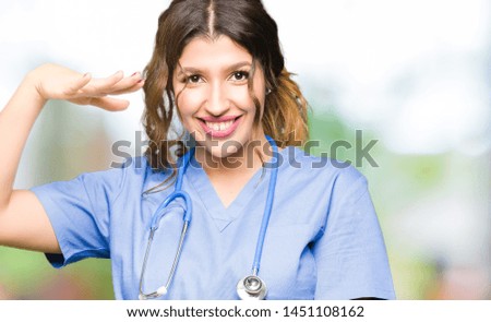 Young adult doctor woman wearing medical uniform gesturing with hands showing big and large size sign, measure symbol. Smiling looking at the camera. Measuring concept.