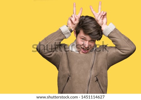 Young handsome man wearing winter coat over isolated background Posing funny and crazy with fingers on head as bunny ears, smiling cheerful