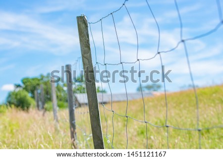 Metal wire farm fence with barn and blue sky in background