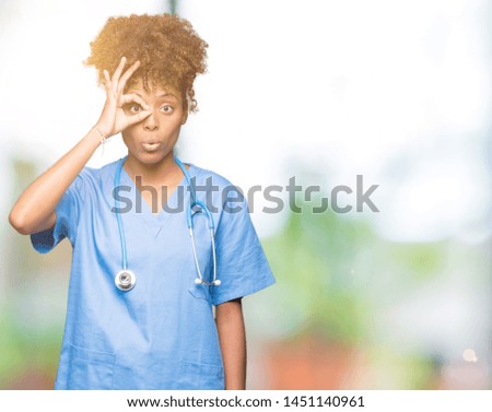 Young african american doctor woman over isolated background doing ok gesture shocked with surprised face, eye looking through fingers. Unbelieving expression.