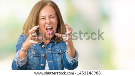 Beautiful middle age woman wearing casual denim jacket over isolated background Shouting frustrated with rage, hands trying to strangle, yelling mad