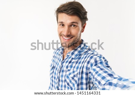 Image of a optimistic happy young unshaved man dressed in casual shirt posing isolated over white wall background take a selfie by camera.