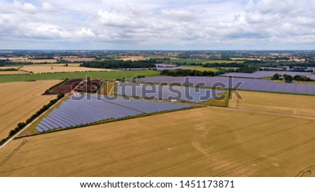 An aerial view of a large solar farm, in the centre of farmland, reflecting in the sun.