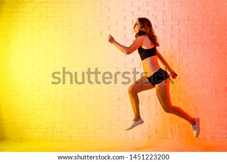 Young athletic woman jumping over a yellow background. Dynamic movement. Sport and active lifestyle.