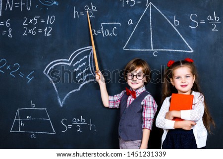 Intelligent smart happy schoolboy and schoolgirl playing in mathematic teacher opposite school chalkboard at school in classroom with school books and notebooks. Back to school, ready to study concept