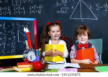 Intelligent smart happy schoolboy and schoolgirl playing in mathematic teacher opposite school chalkboard at school in classroom with school books and notebooks. Back to school, ready to study concept