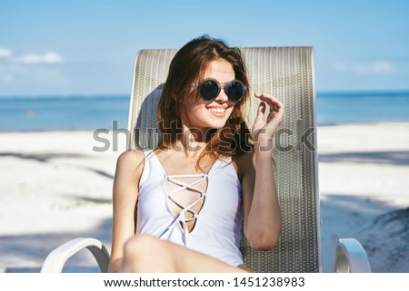 Beautiful woman in sunglasses white swimsuit chaise longue sand ocean sea                       