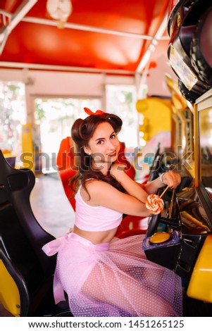 beautiful brunette girl in pin-up style in a white skirt with candy with slot machines in colored lights. plays, presses a button, rests. emotions joy smile
