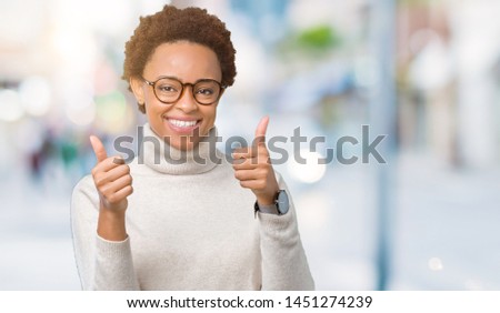 Young beautiful african american woman wearing glasses over isolated background success sign doing positive gesture with hand, thumbs up smiling and happy. Looking at the camera
