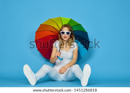  woman in glasses sits on the floor with an umbrella on a blue background                              