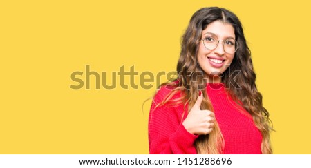 Young beautiful woman wearing red glasses doing happy thumbs up gesture with hand. Approving expression looking at the camera with showing success.