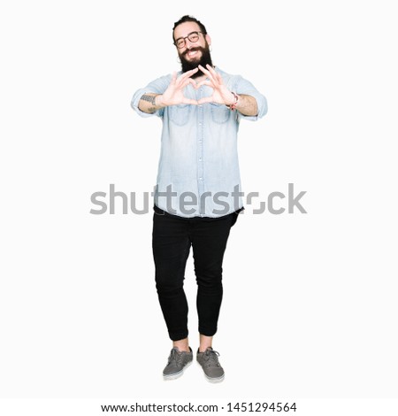 Young hipster man with long hair and beard wearing glasses smiling in love showing heart symbol and shape with hands. Romantic concept.