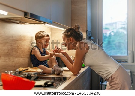 Preparation of a family breakfast. mother and baby son cook porridge in morning. Mother and son preparing food in kitchen together. Funny little baby boy with mom on kitchen.