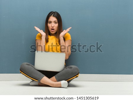 Young woman sitting on the floor with a laptop surprised and shocked