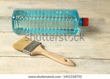 A brush lies next to a transparent plastic bottle with a solvent on an old white vintage wooden plank table. Place for text or logo.