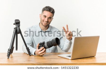Young handsome photography teacher showing victory sign and smiling broadly.